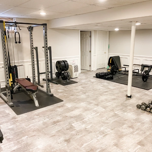 The gym flooring is a mix of a light-colored wood-look floor and black rubber mats under the heavy equipment